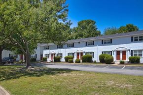 Newport News townhouse for rent - A white building with red doors and windows is surrounded by greenery.
