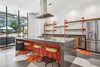 The kitchen has a large island with orange stools and stainless steel appliances