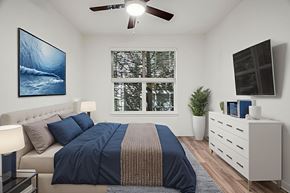 Hillsboro apartment for rent - A bedroom with a bed, a ceiling fan, a window with a view of trees, a nightstand with a lamp, and a painting on the wall.