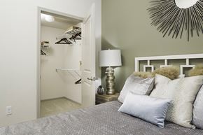 Vista apartment for rent - A bedroom with a bed, lamp, and a closet with clothes hanging.