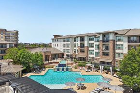 Englewood apartment for rent - A large swimming pool surrounded by lounge chairs and umbrellas in front of a multi-story apartment building.