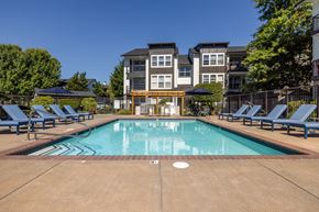 Mukilteo apartment for rent - a swimming pool with chaise lounge chairs and umbrellas in front of an apartment building