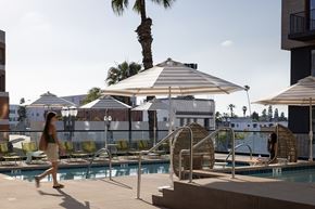 Long Beach apartment for rent - A woman is walking past a pool with a palm tree in the background.
