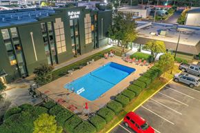 Greenville apartment for rent - A swimming pool is surrounded by a hedge and a red van is parked in the parking lot.