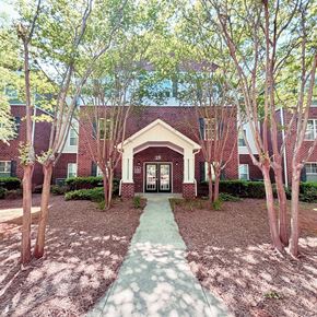 Greenville apartment for rent - A red brick building with a white door and a green pathway leading to it.
