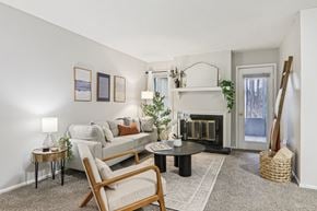 Greenville apartment for rent - Plantations at Haywood staged living room with carpet, couch, ladder blanket, chairs and attached kitchen.