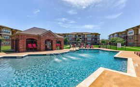 Hewitt apartment for rent - A large swimming pool in front of a brick building with a black fence around it.