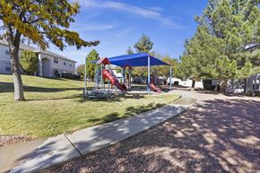 El Paso apartment for rent - A playground with a red slide and a blue canopy is surrounded by a gravel path and trees.