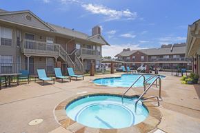 Oklahoma City apartment for rent - A swimming pool surrounded by chairs and a building in the background.