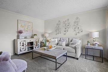 Oklahoma City apartment for rent - A living room with a white couch, a grey armchair, a coffee table, and a painting on the wall.