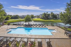 Oklahoma City apartment for rent - A large outdoor swimming pool surrounded by a black fence and lounge chairs.