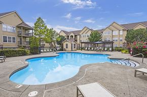 Owasso apartment for rent - A large swimming pool surrounded by a concrete patio and a black fence.