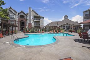 Yukon apartment for rent - A large outdoor swimming pool surrounded by a patio with chairs and a building in the background.