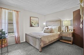 Wichita apartment for rent - A bedroom with a large bed and a small table with a plant on it.