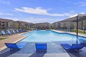 Maize apartment for rent - A large swimming pool with blue lounge chairs and a black umbrella.