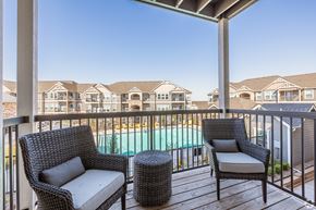 Norman townhouse for rent - A balcony with two chairs and a table overlooking a pool.