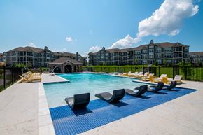 Belton apartment for rent - A large swimming pool with lounge chairs in front of a multi-story building.