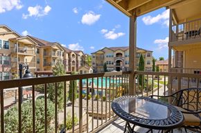 Waco apartment for rent - A balcony with a table and chairs overlooks a pool and apartment buildings.