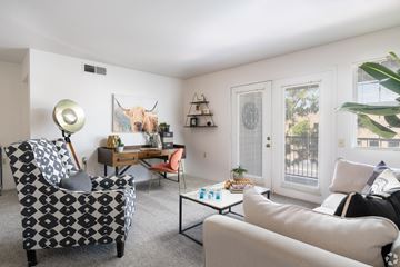 El Paso apartment for rent - A living room with a patterned chair, a white couch, and a painting of a bull on the wall.
