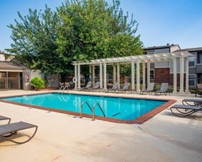 Oklahoma City apartment for rent - A pool with a white pergola and chairs around it.