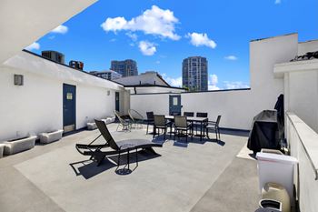 Rooftop patio with chairs, a table, and bbq is shown with a blue sky in the background.