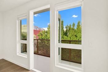 A room with two windows overlooking a red building and green trees