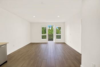 A large empty room with a dishwasher on the left and a window with a view of trees outside