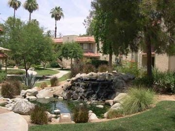 Palm Desert apartment for rent - A garden with a waterfall and a house in the background.