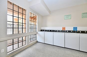 A room with a row of white cabinets and a window with bars on the left side.