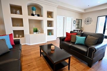 Mesa apartment for rent - A black leather couch with red and blue pillows sits in a living room with a black coffee table and white shelves with decorative items.