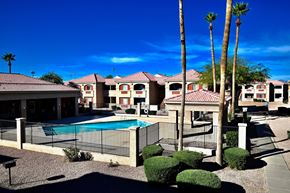 Mesa apartment for rent - A pool surrounded by a black fence and palm trees.