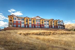 Castle Rock apartment for rent - A large multi-story building with a red and yellow facade sits on a hill.