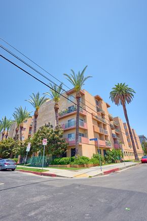 Los Angeles apartment for rent - A street view of a residential area with a building, palm trees, and a car.