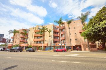 Los Angeles apartment for rent - A red car is parked on the side of the road in front of a building.