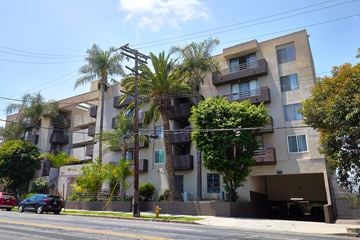 Los Angeles apartment for rent - A black car is driving down a street past a building with balconies.