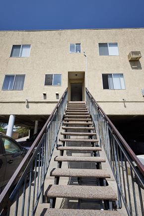 Los Angeles apartment for rent - A staircase with a metal railing leads up to a doorway in a tan building.
