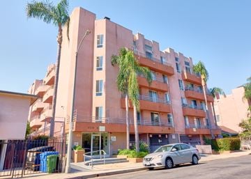 Los Angeles apartment for rent - A silver car is parked in front of a pink building with palm trees.