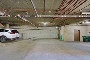 Los Angeles apartment for rent - A car is parked in a garage with a wall of pipes running along the ceiling.
