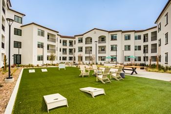 A grassy courtyard with chairs and tables in front of apartment buildings.
