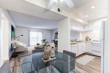 A living room with a glass table and a kitchen in the background