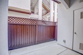 A balcony with a wooden fence and a white building with a staircase in the background