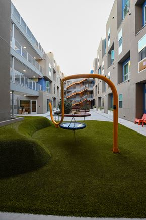 Santa Monica apartment for rent - A playground with a swing set in the middle of a grassy area in front of apartment buildings.