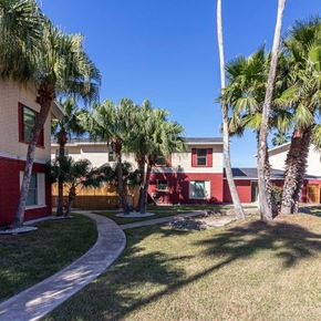 Harlingen apartment for rent - A red building with a white fence and palm trees in front.