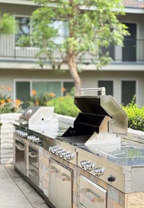 Tustin apartment for rent - A BBQ grill with a clear lid is in front of a building with a tree and flowers in the background.