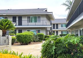 Tustin apartment for rent - A building with a balcony and a black door is surrounded by green plants.