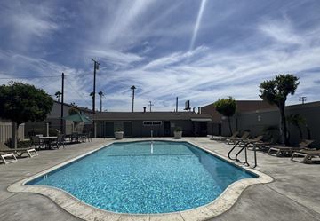 Garden Grove apartment for rent - A large outdoor swimming pool with lounge chairs and a building in the background.