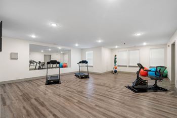 A gym with treadmills and weights in a room with white walls and floors