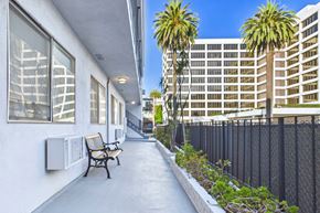 Beverly Hills apartment for rent - A long concrete walkway with a bench and a fence on the right side.
