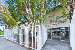 North Hollywood apartment for rent - A white fence surrounds a building with a green sign that says Ques.