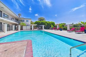 Van Nuys apartment for rent - A swimming pool in front of a building with red chairs around it.
